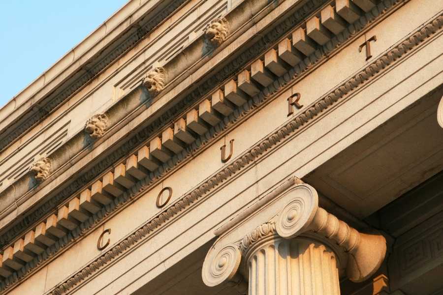 Vue en contre-plongée de la façade en pierre d'un bâtiment juridique affichant le mot COURT en lettres dorées.