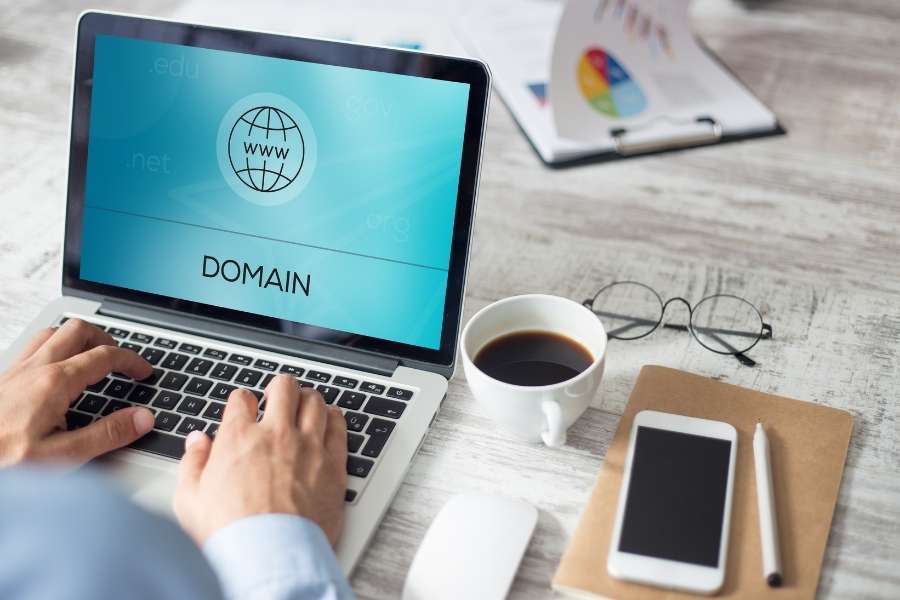 Un utilisateur tape sur le clavier d'un ordinateur portable affichant un écran bleu dédié à la recherche de nom de domaine.