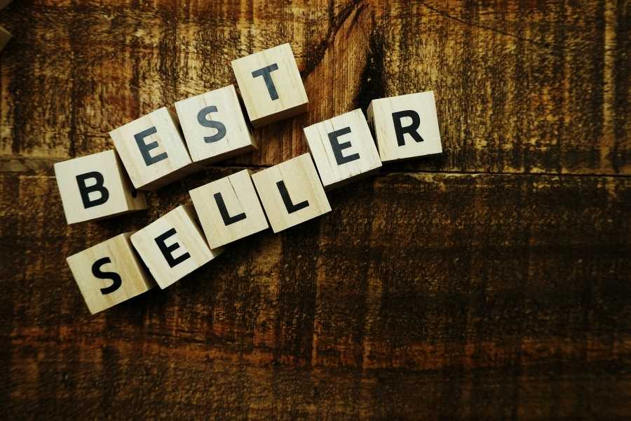 Des cubes en bois affichant les lettres du mot BEST SELLER sont disposés en diagonale sur une table en bois marron foncé.