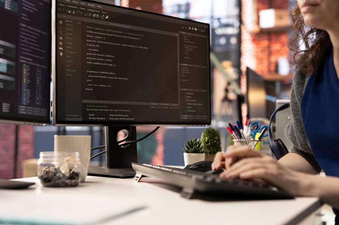 Gros plan sur une développeuse qui tape sur son clavier devant deux grands écrans affichant du code. Idéal pour une entreprise cherchant à créer un site.