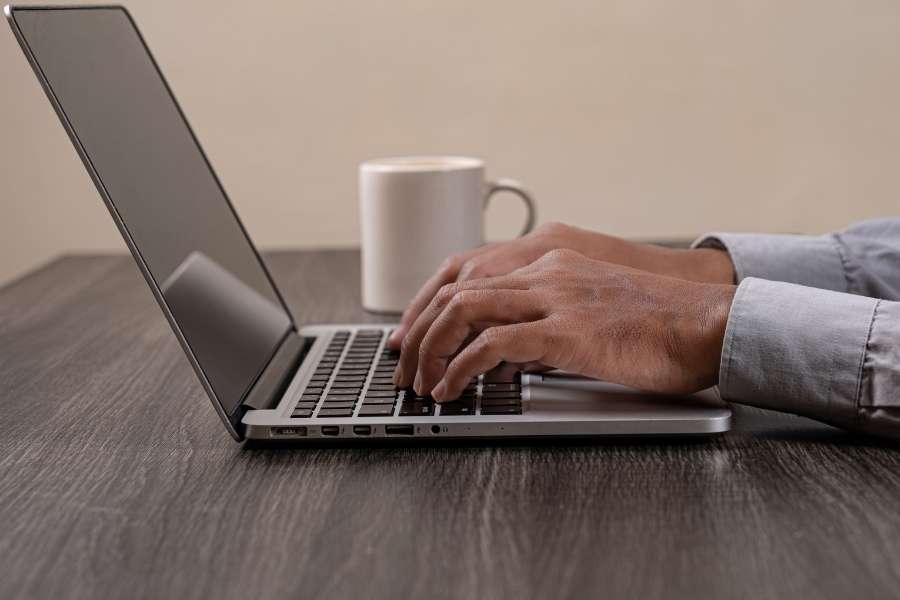 Un rédacteur tape sur le clavier de son ordinateur portable à côté d'une tasse de café, illustrant une session de travail pour booster la créativité des rédacteurs.